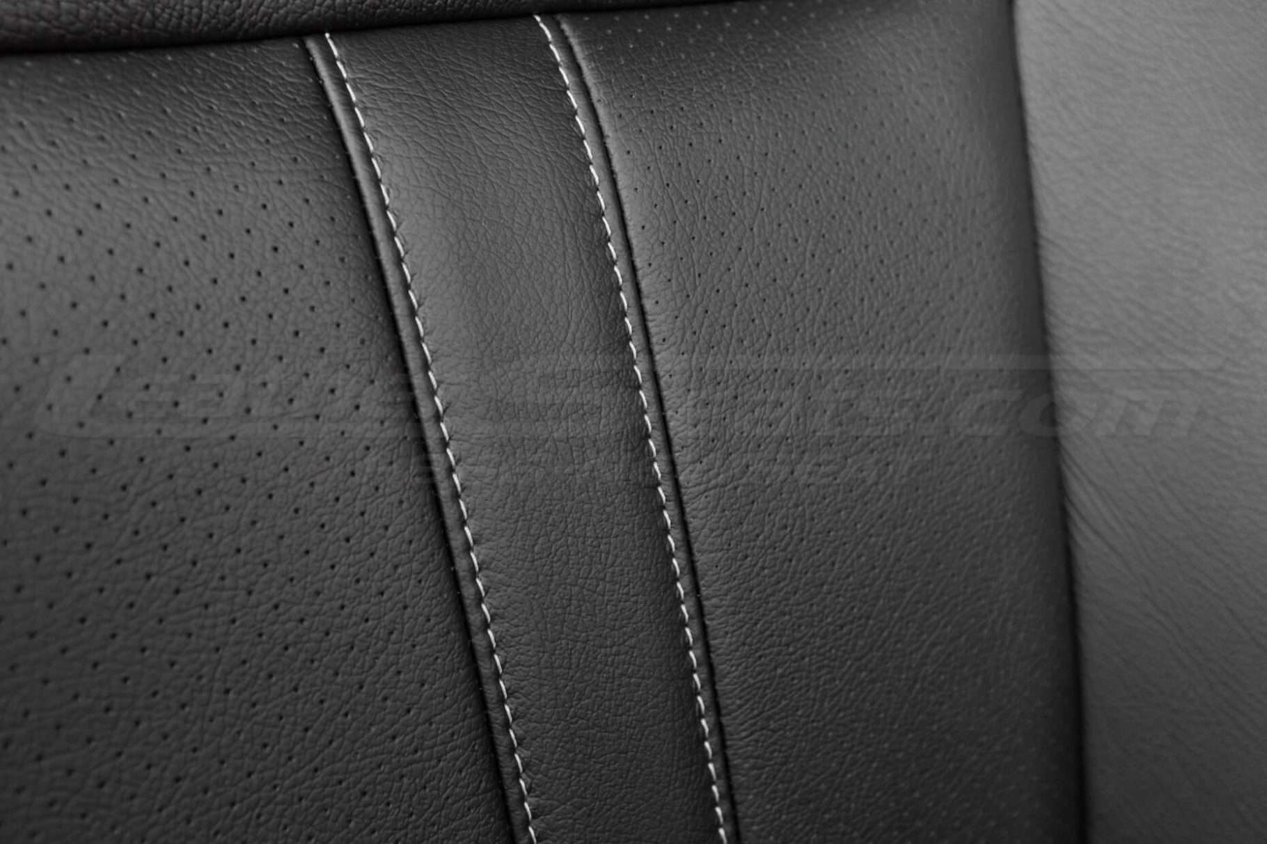 Contrasting double-stitching in stone and perforated inserts on black leather close-up