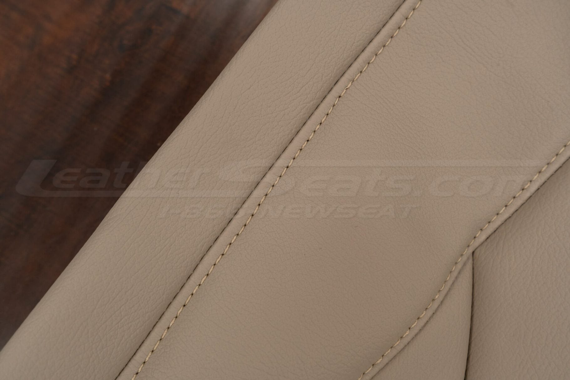 Close-up of beige leather seat cover with double-stitched seam and fine grain texture.